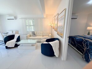 A modern living room with a sofa, armchairs, a coffee table, and a bed with a patterned bedspread. - Short Walk to Beach • 3BR Poolside Unit • Next to Nature Preserve (Fort Myers Beach)