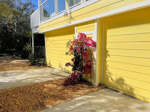 A yellow building with a garage door, a concrete driveway, and a small garden with pink flowers. - Big Groups,Nature View Estates 3 units private pool, WALK TO BEACH (Fort Myers Beach)