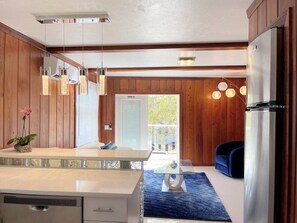 A modern kitchen with wooden paneling, a central island, and a view to an outdoor balcony. - Big Groups,Nature View Estates 3 units private pool, WALK TO BEACH (Fort Myers Beach)