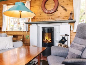 A cozy room with a fireplace, a wooden wall, a table, and a comfortable chair. - 8 Person Holiday Home in Martofte (Martofte)