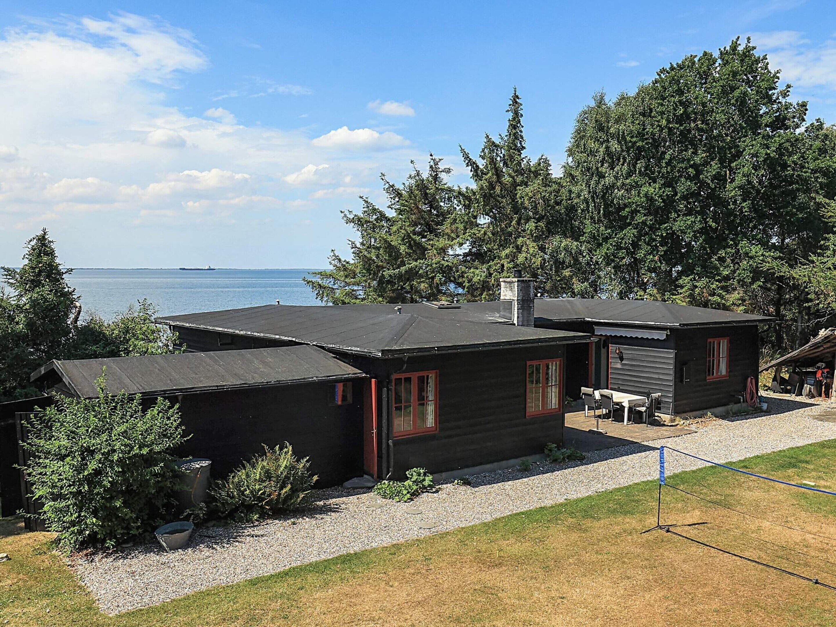 A cabin with a gravel driveway, a small patio, and a view of the water.