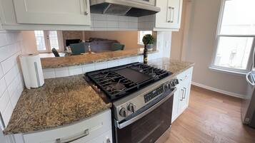 A kitchen with white cabinets, a granite countertop, a stainless steel stove, and an oven.