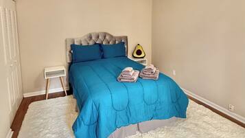 A bedroom with a bed, a ceiling fan, a nightstand, and a white fluffy rug.