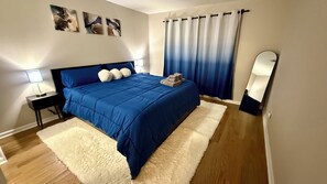 A bedroom with a bed, bedside lamps, a large window with curtains, and a mirror.