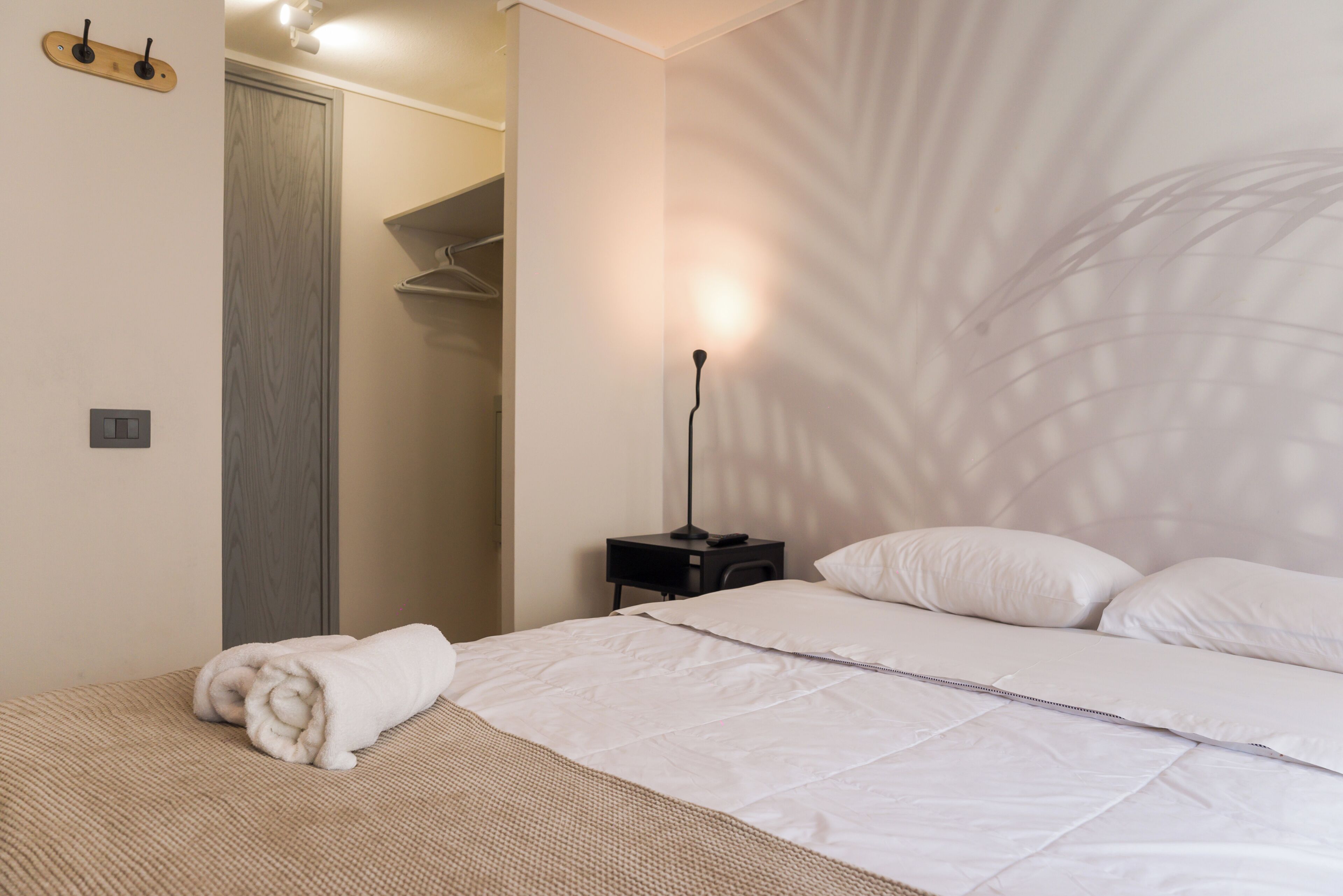 A neatly made bed with white linens, a bedside table with a lamp, and a towel on the floor.