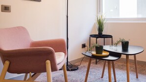 A modern living room with a pink sofa, a floor lamp, a small table with a potted plant, and a large window. - Eleuterio Ramirez Apartments by Andes (Santiago)
