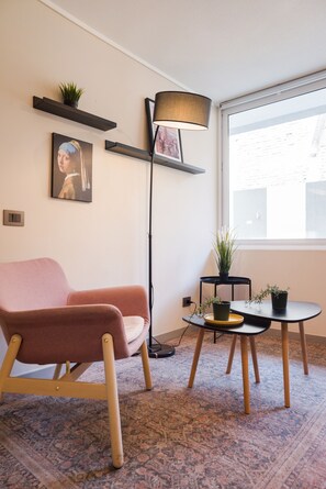 A modern living room with a pink sofa, a floor lamp, a small table with a potted plant, and a large window. - Eleuterio Ramirez Apartments by Andes (Santiago)