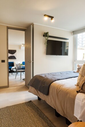 Un dormitorio moderno con cama, televisor montado en la pared y puerta que da a un comedor.