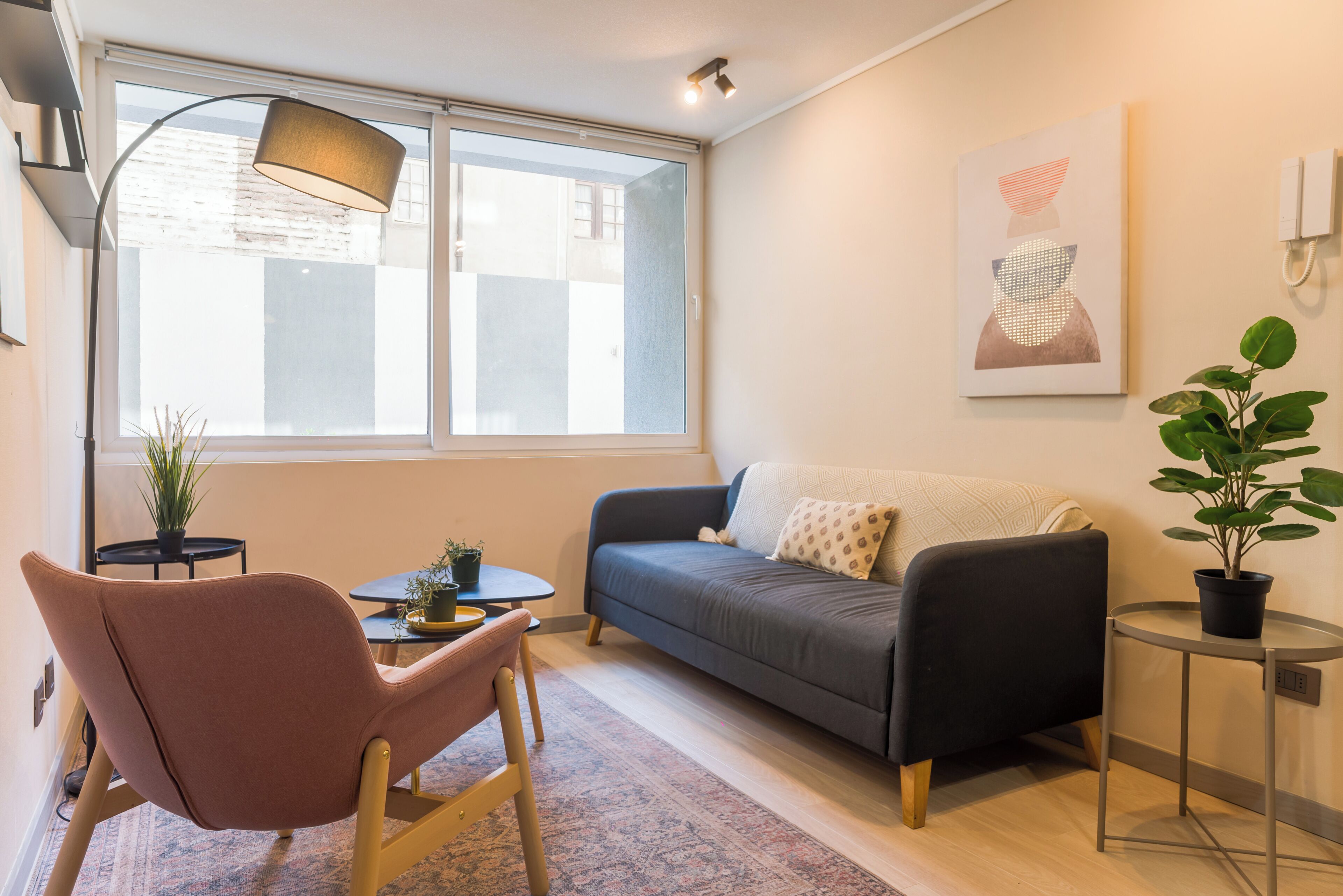 Un salon moderne comprenant un canapé, un fauteuil, une petite table, une lampe et une fenêtre avec des stores.