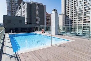 Una piscina en la azotea con terraza de madera, rodeada de edificios modernos.