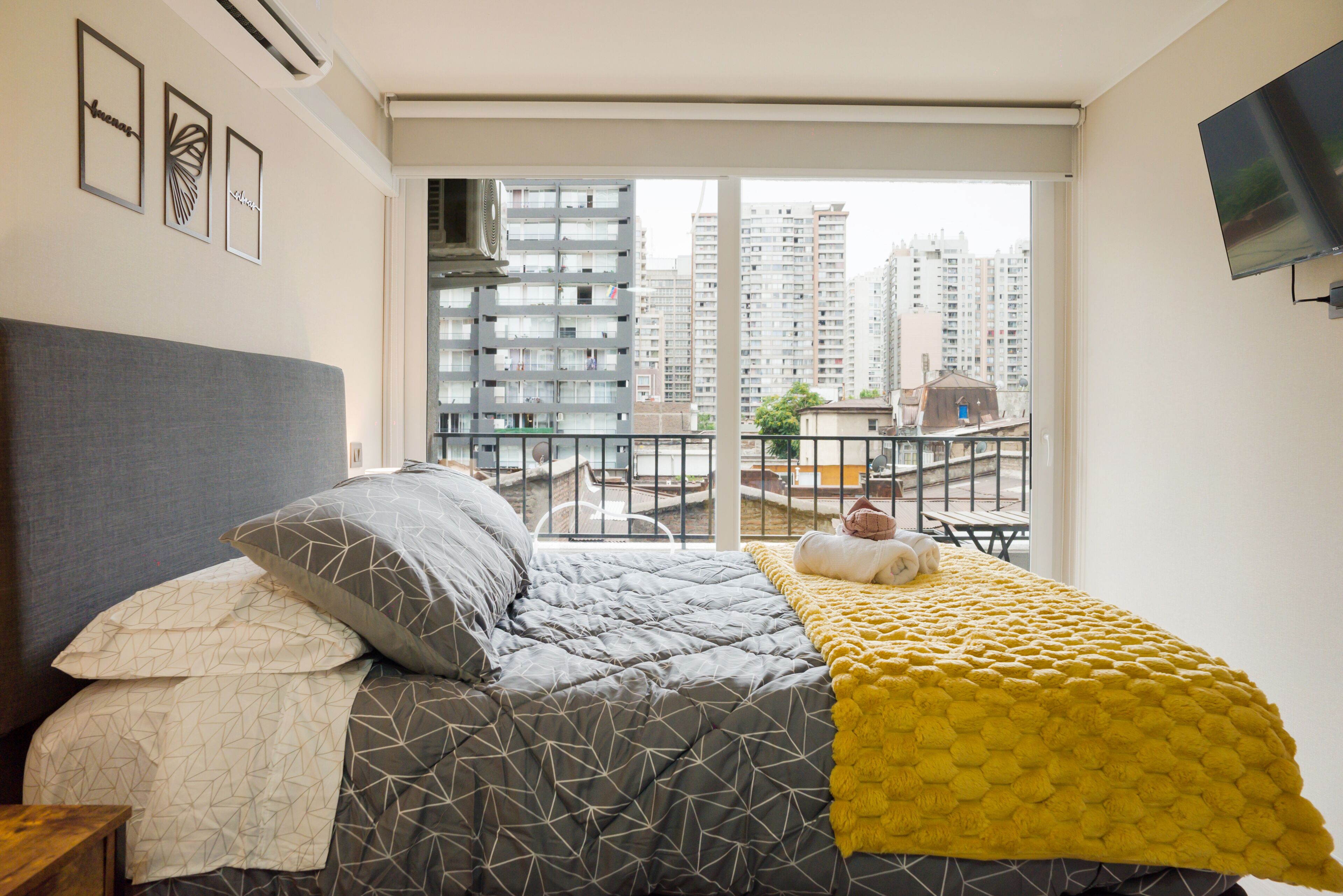 Un dormitorio con cama, ventana y vistas a edificios altos.