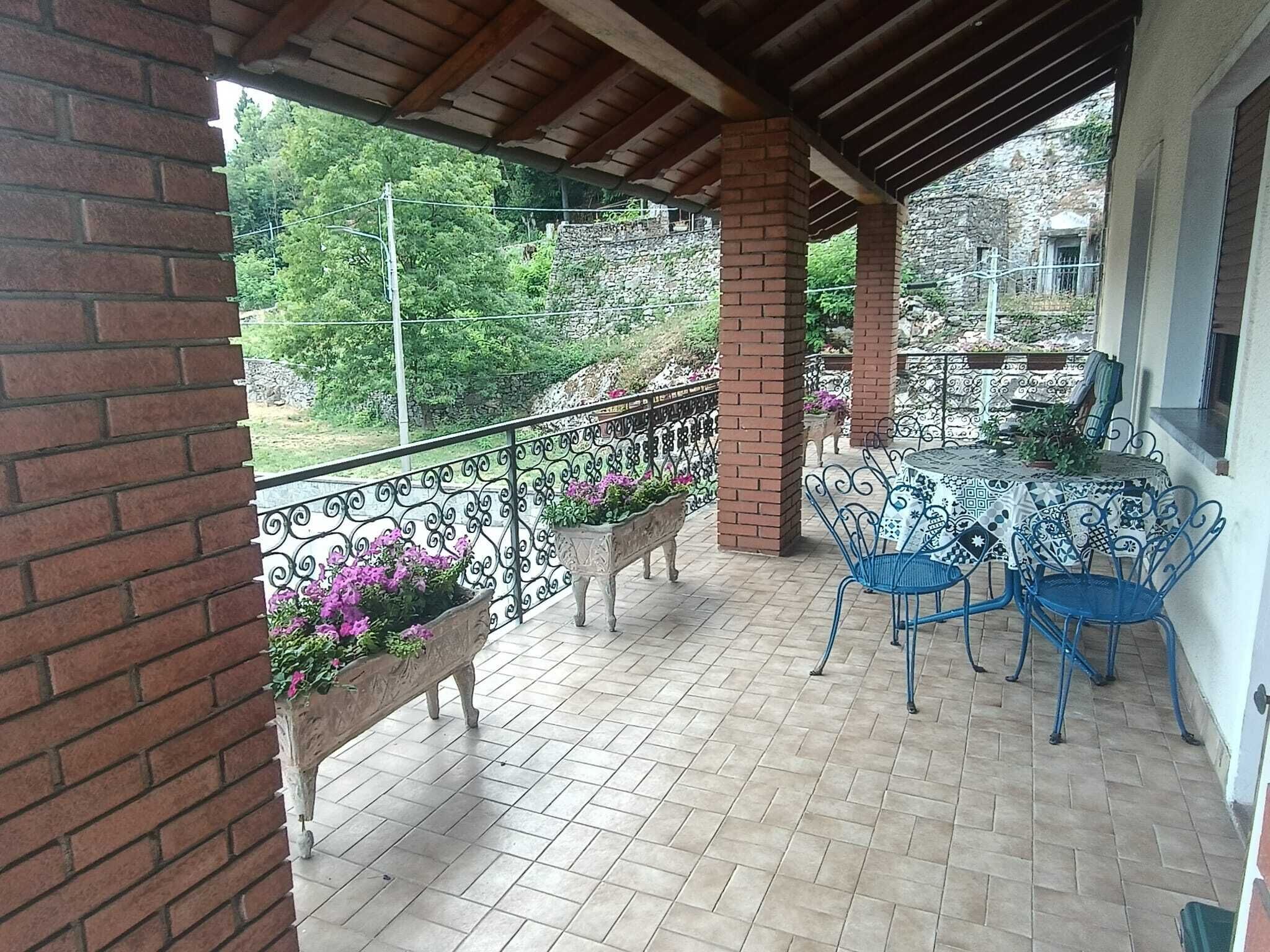 Een overdekt terras met een bakstenen muur, een metalen hekwerk en een tafel met stoelen.