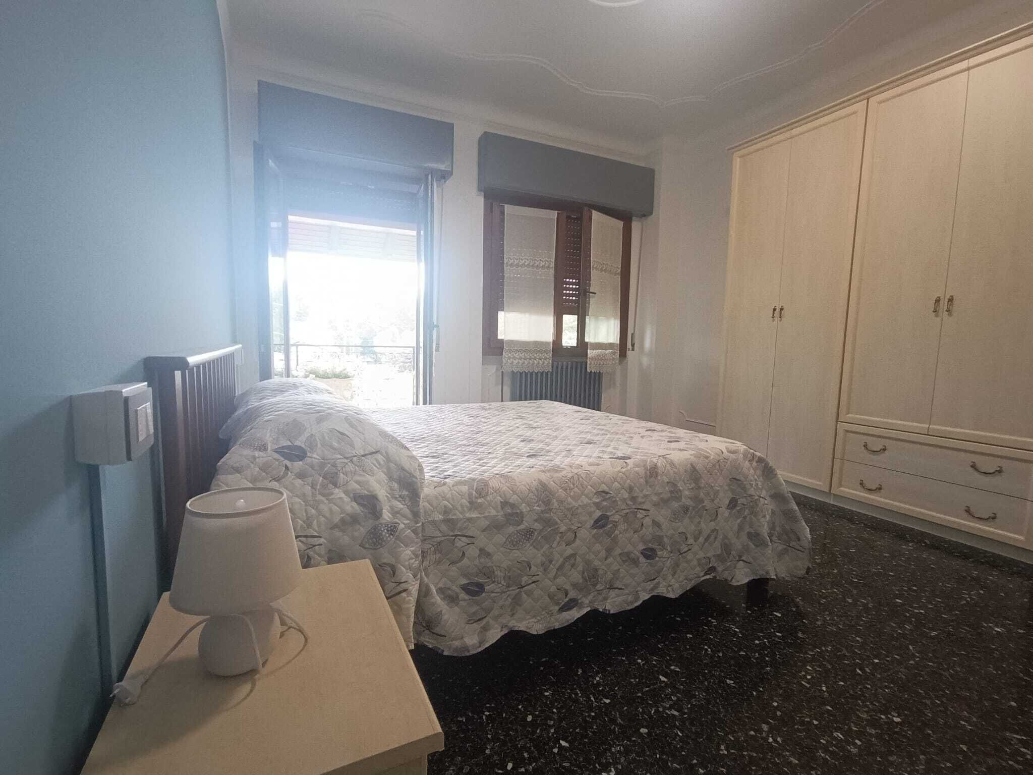 A bedroom with a bed, a bedside table with a lamp, a wardrobe, and a window with curtains.