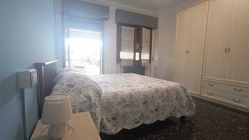 A bedroom with a bed, a bedside table with a lamp, a wardrobe, and a window with curtains.