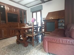 A dining area with a wooden table and chairs, a pink vase, and a leather sofa.