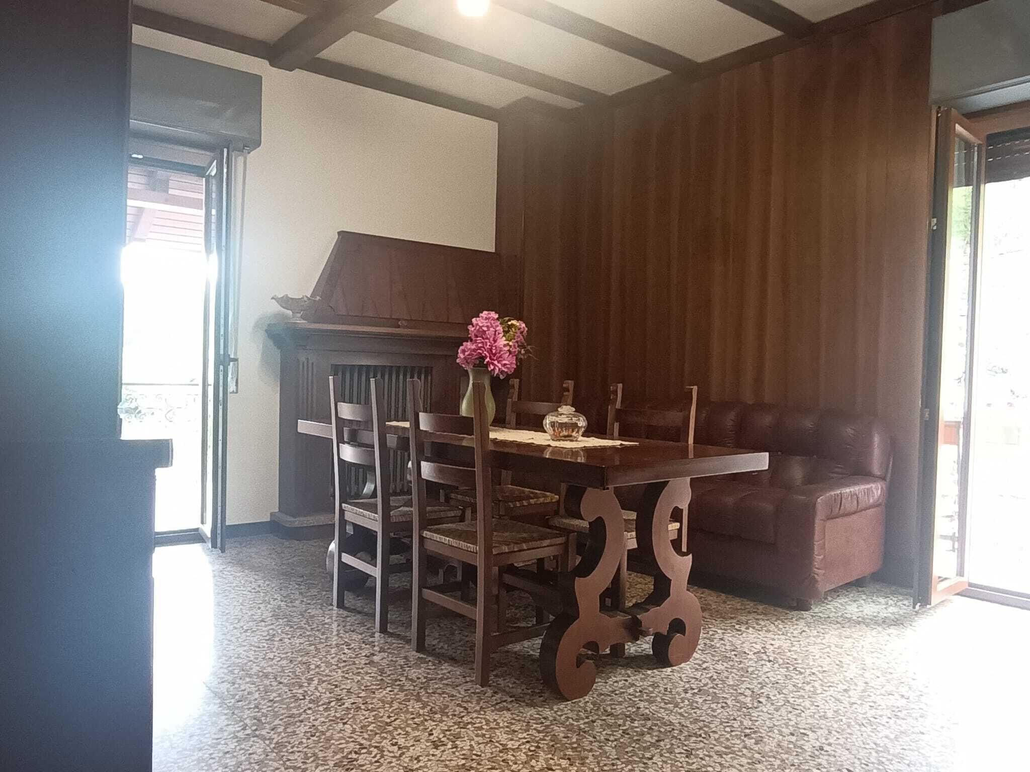 Een eetruimte met een houten tafel, stoelen, een vaas met bloemen, een piano en een leren bank.