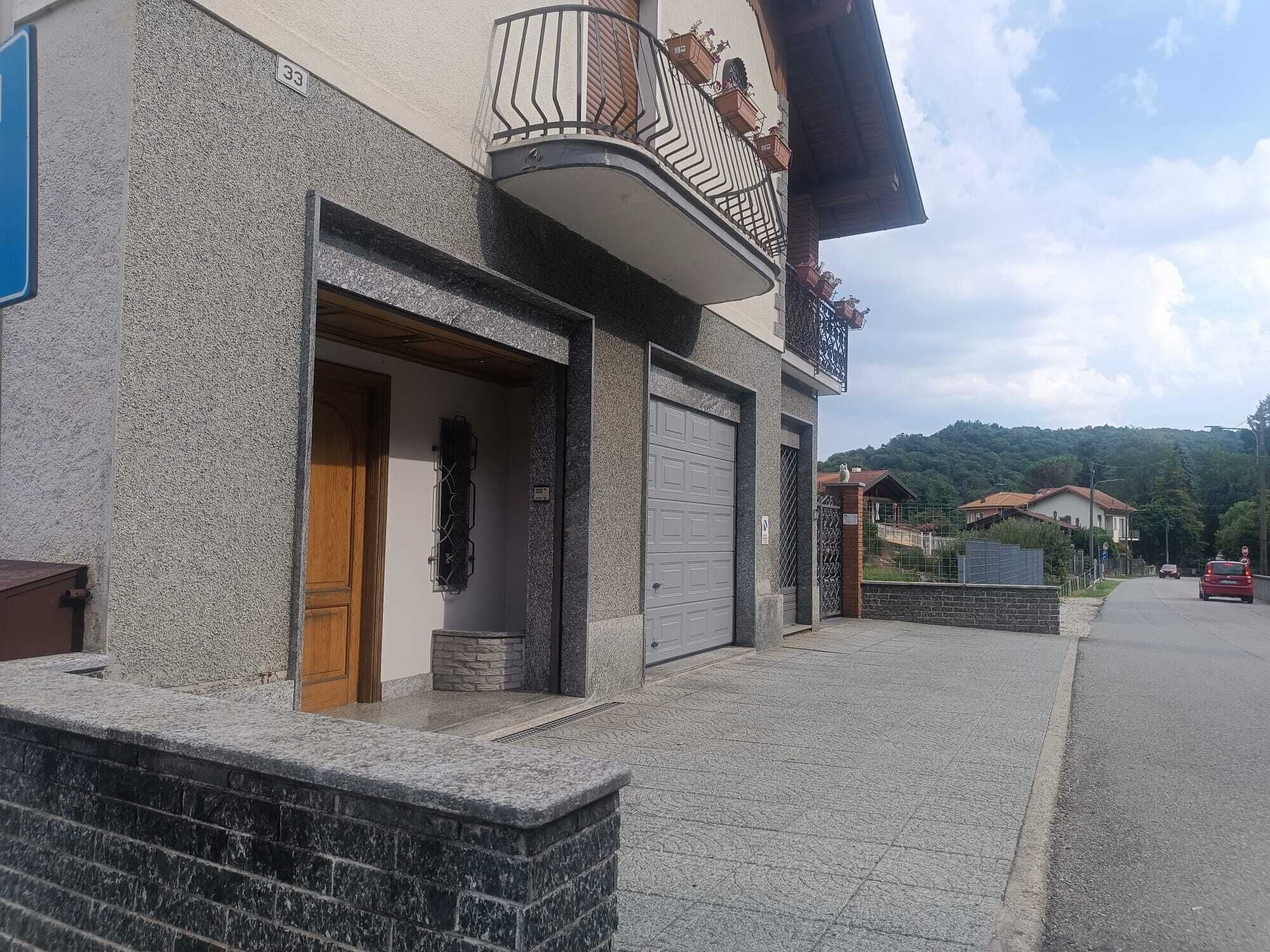 Un immeuble résidentiel avec une façade en pierre, une porte en bois, un garage et un balcon agrémenté de plantes en pot.