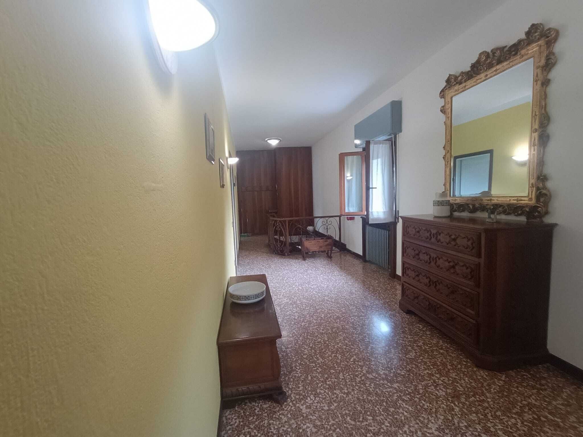 Een gang met een houten dressoir, een spiegel en een deur naar een andere kamer.
