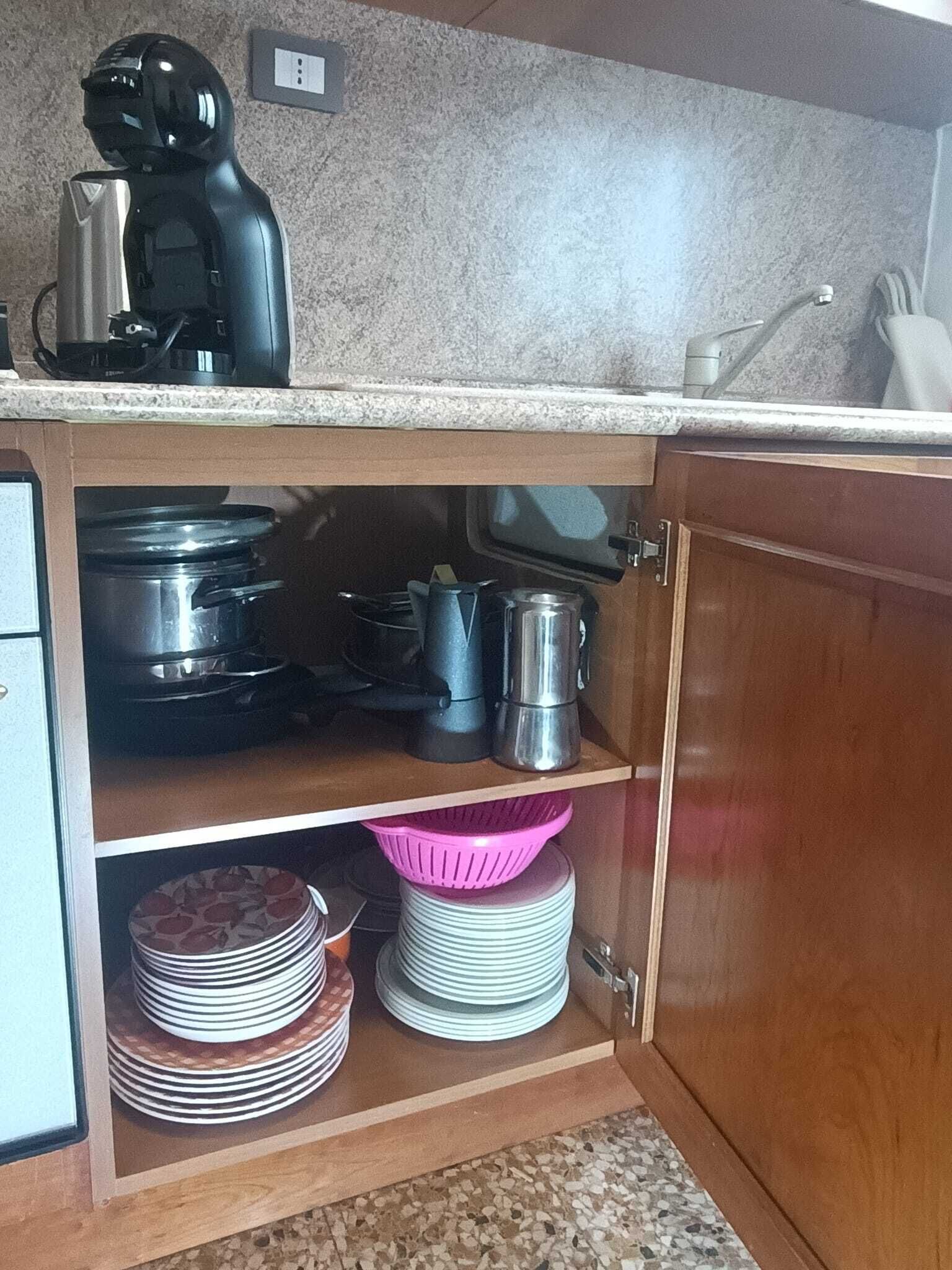 Een keuken met een koffiezetapparaat, pannen en een stapel borden.