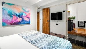 A modern bedroom with a large abstract painting, a bed with a patterned bedspread, a television mounted on the wall, and a wooden door leading to another room. - Rosa and Noir Riverside Escape near Botanic Gardens (South Yarra)