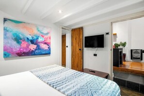 A modern bedroom with a large abstract painting, a bed with a patterned bedspread, a television mounted on the wall, and a wooden door leading to another room. - Rosa and Noir Riverside Escape near Botanic Gardens (South Yarra)