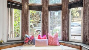 A bay window with four panes, a cushioned bench with pillows, and a view of greenery and parked cars outside. - Rosa and Noir Riverside Escape near Botanic Gardens (South Yarra)