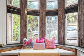 A bay window with four panes, a cushioned bench with pillows, and a view of greenery and parked cars outside. - Rosa and Noir Riverside Escape near Botanic Gardens (South Yarra)