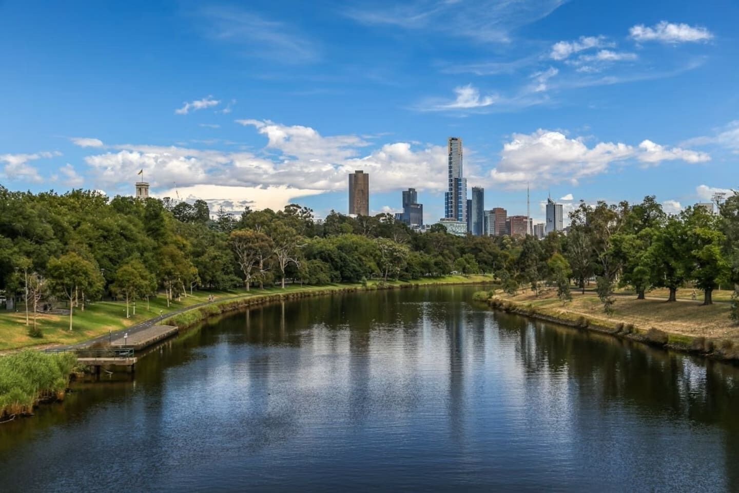 A river with a city skyline in the background, surrounded by trees and greenery.