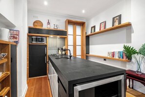 Uma cozinha moderna com uma ilha central, estantes de madeira e forno embutido.