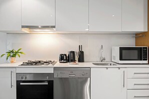 Een moderne keuken met witte kasten, een gasfornuis, een vaatwasser, een magnetron en een spoelbak.