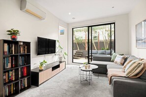 Ein modernes Wohnzimmer mit Flachbildfernseher, Bücherregal, grauem Sofa und einem kleinen runden Couchtisch.