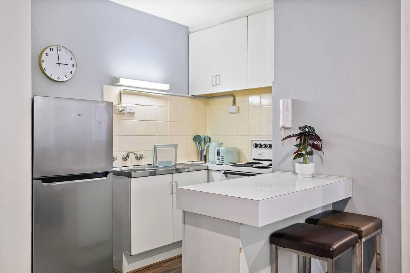 A compact kitchen with a refrigerator, stove, sink, and a clock on the wall.