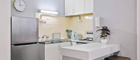 A compact kitchen with a refrigerator, stove, sink, and a clock on the wall.
