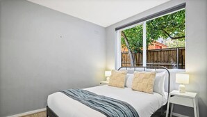 Une chambre à coucher avec un lit, des tables de chevet et une fenêtre donnant sur une clôture en bois et des arbres.