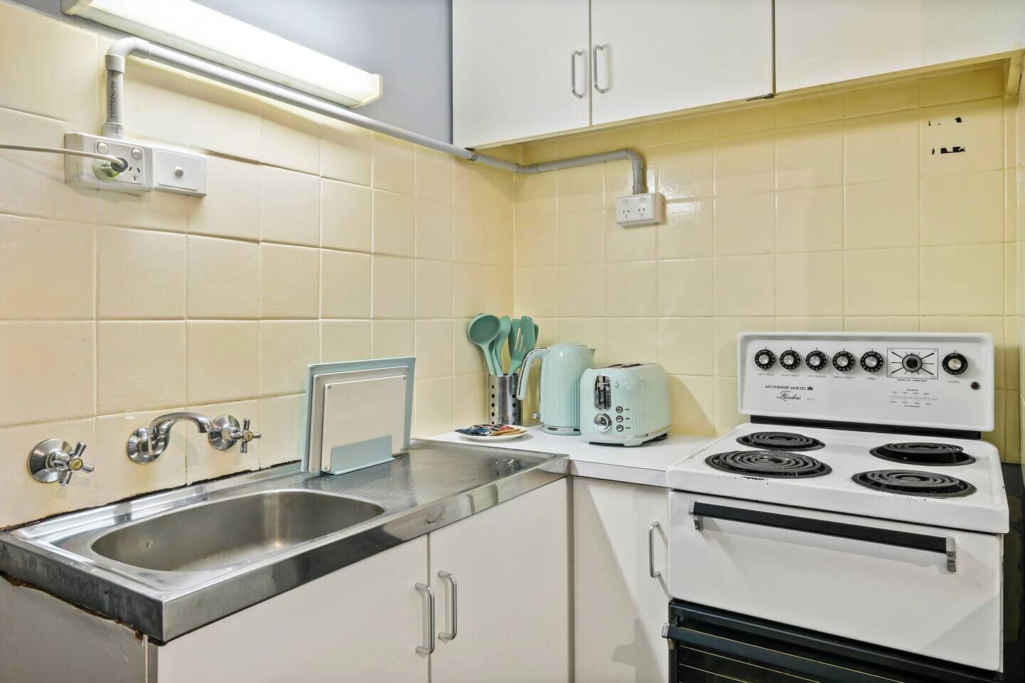 A compact kitchen with a sink, a stove, and a toaster. There are cabinets and a countertop.