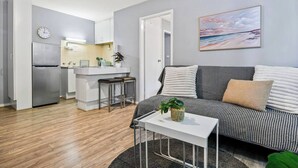 Un salon moderne comprenant un canapé, une petite table et un coin cuisine avec un réfrigérateur et un évier.