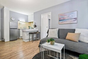 A modern living room with a sofa, a small table, and a kitchen area with a refrigerator and a sink. - Richmond Pad MCG and Bridge Rd Stay Free Parking (Richmond)