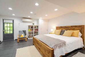 Quarto com uma cama grande, uma estante de livros, uma cadeira e uma porta com janela.