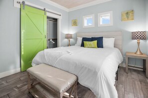 A bedroom with a bed, bench, bedside lamps, and a green sliding door. - Coastal Escape - Beach Access - Pet Friendly (Bolivar Peninsula)