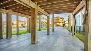 An open wooden structure with a concrete floor, columns, and a view of residential buildings in the background. - Coastal Escape - Beach Access - Pet Friendly (Bolivar Peninsula)