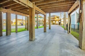 An open wooden structure with a concrete floor, columns, and a view of residential buildings in the background. - Coastal Escape - Beach Access - Pet Friendly (Bolivar Peninsula)