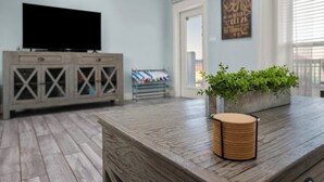 A room with a wooden floor, a television on a cabinet, and a plant on a table. - Coastal Escape - Beach Access - Pet Friendly (Bolivar Peninsula)