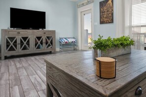 A room with a wooden floor, a television on a cabinet, and a plant on a table. - Coastal Escape - Beach Access - Pet Friendly (Bolivar Peninsula)