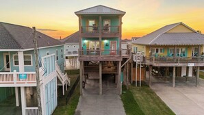 A multi-story building with a balcony on the second floor, a covered front porch, and a small deck area. - Coastal Escape - Beach Access - Pet Friendly (Bolivar Peninsula)