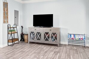 A room with a television on a wooden cabinet, a ladder, a basket, and a clothes drying rack. - Coastal Escape - Beach Access - Pet Friendly (Bolivar Peninsula)