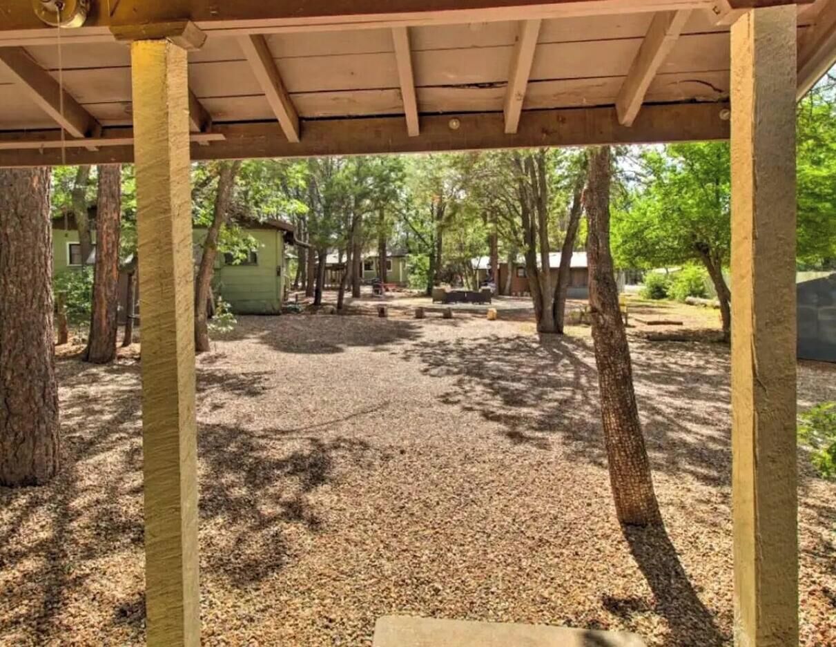 A covered outdoor area with a gravel surface, surrounded by trees and a small building.