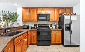 A kitchen with wooden cabinets, a microwave, a stove, a refrigerator, and a sink. - Oceanfront Condo with Shared Pool & Fitness Room (Destin)