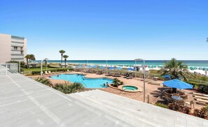 A resort pool area with multiple swimming pools, lounge chairs, and umbrellas, overlooking a beach and ocean. - Oceanfront Condo with Shared Pool & Fitness Room (Destin)