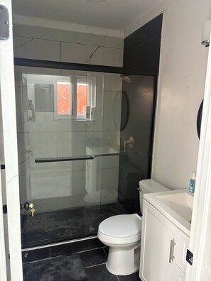 A bathroom with a glass-enclosed shower, a white toilet, and a sink with a mirror. - Cozy 1-bedroom house in wonderful Nassau with AC and outdoor fitness area (Nassau)