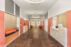 Um saguão de hotel com balcão de recepção, área de estar e um corredor que leva à entrada.